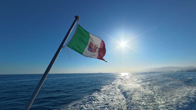 Italian flag flying above a boat wake on a sunlit sea