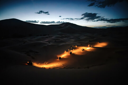 Quad bikes driving across erg chebbi sand dunes, illuminating their path with headlights during a desert adventure at twilight