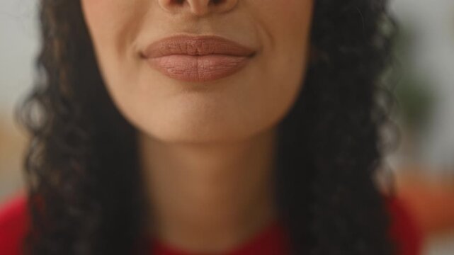 Woman puckers lips in a gentle kissing motion showing full lower face, smile lines and curly hair framing chin in a studio setting; playful flirtation.