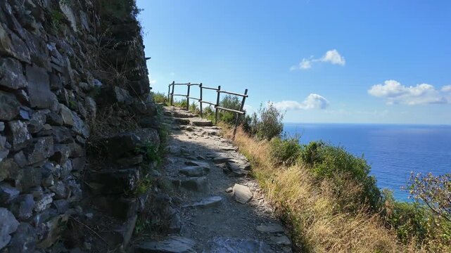 Rocky cliff path with wooden railing beside blue sea. Hiking in Cinque Terre
