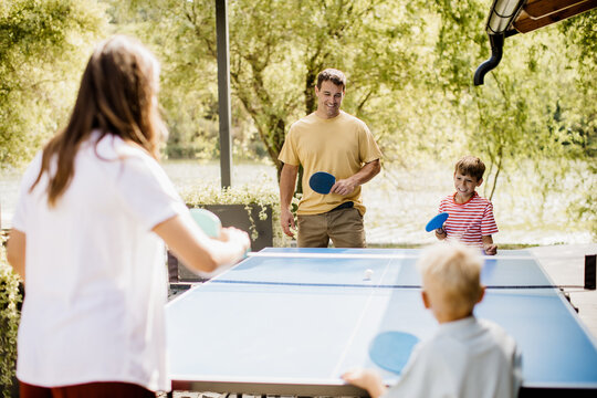 Family enjoying a sunny day playing table tennis by the lakeside