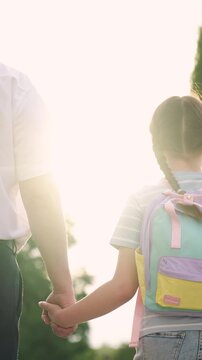 girl child kid walks holding father hand sun glare, book hand, hold textbook hand, kid child carries school textbook hand, man father leads student backpack by hand, happy family, education child sun