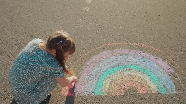 child kid girl baby draws rainbow pavement chalk, childhood dream. Girl draws a rainbow, She uses bright chalk, Sitting on warm pavement, The sun is shining, Her dress sways gently, She is focused
