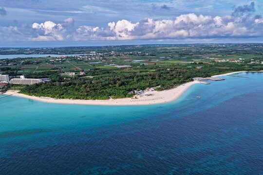 Aerial view of Yonaha Beach with its pristine white sand, turquoise waters, and lush coastal vegetation under a bright blue sky in Miyakojima, Okinawa, Japan.