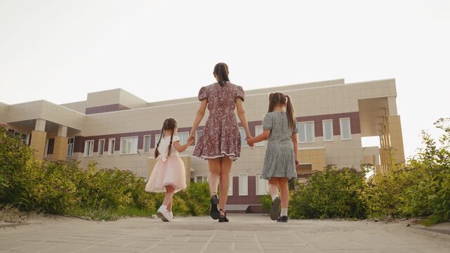 Woman and children approach a building, Dressed in pretty outfits, Twins or siblings, Back to school, Educational institution, Mother s care, Urban architecture, Bright afternoon, United family