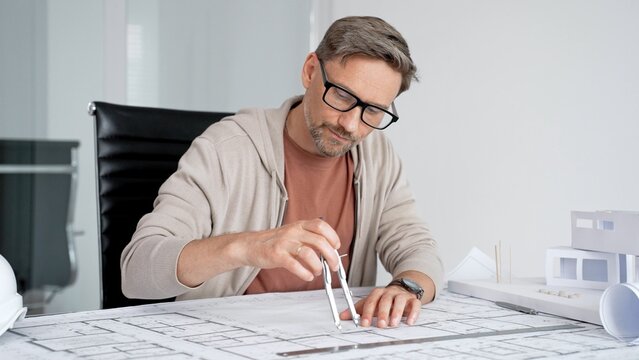 Architect man working on new building blueprint plans, drawing details with a compass, designing residential and commercial projects for clients