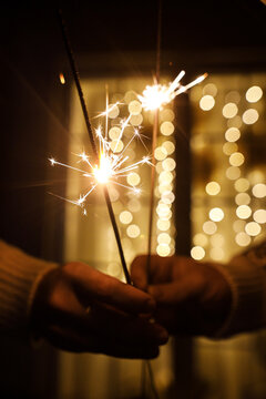 Couple Holding Burning Sparklers with Warm Bokeh Lights Background. Christmas magic and wonder. Burning fireworks on New Year Eve. Vertical Shot