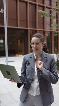 Businesswoman talking to camera holding a laptop computer outdoors