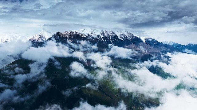 High-altitude view of rugged mountain peaks covered in snow and shrouded by low-hanging clouds under soft, diffused natural daylight.