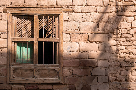 Close-up view of an antique traditional wooden window with iron bars set in an authentic mud brick and stone wall in AlUla old town