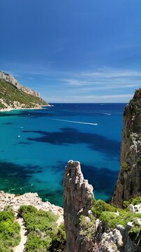 Aerial drone footage of Pedra Longa along the spectacular Baunei Coast in Sardinia, Italy, on a sunny summer day with turquoise sea and clear blue sky