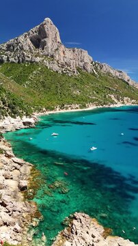 Aerial drone footage of Pedra Longa along the spectacular Baunei Coast in Sardinia, Italy, on a sunny summer day with turquoise sea and clear blue sky
