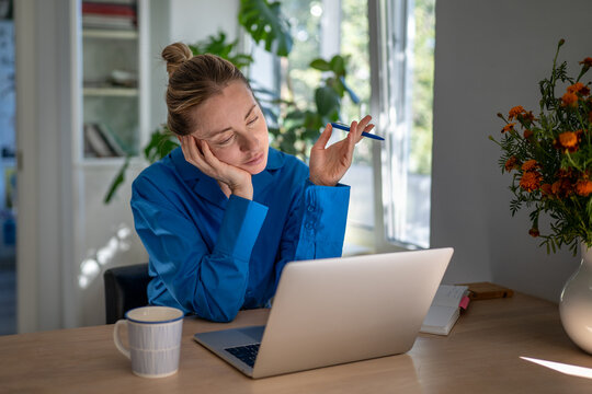 Tired bored woman remote worker exhausted and getting sleepy while working on laptop at home office, uninterested lazy female freelancer staring at computer screen, boredom and slow day at work.