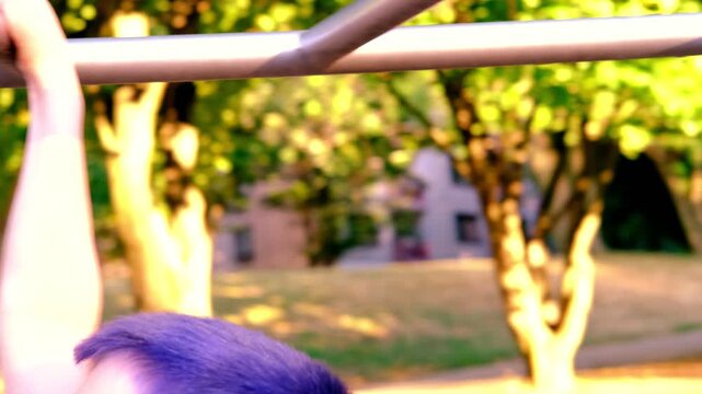 child, boy 8-9 years with blue hair climbing pipes of metal sports projectile, natural green background, concept of cheerful childhood, self-identification, sports achievements, physical development
