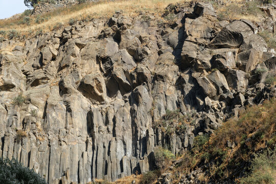 Geological formations of basalt columns in Armenia, with distinct rock textures and patches of vegetation on a sloping hillside