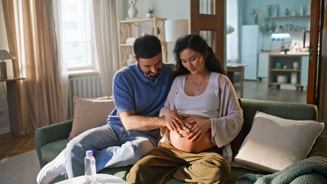 Expectant couple touching pregnant belly sofa. Husband caressing wife stomach.
