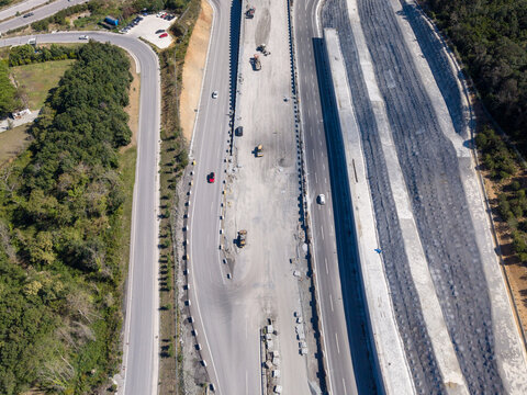 Aerial view of highway construction site with heavy machinery, earthworks, and vehicles driving on adjacent lanes surrounded by green forest in Istanbul, Istanbul, Turkiye.