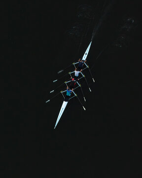 Aerial view of a rowing boat with four rowers gliding across dark water in Poland.