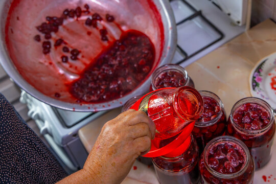 Elderly Person Pouring Homemade Strawberry Preserve into Jars