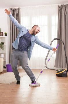 Playful man dances with a mop while doing housework, turning routine floor cleaning into an energetic and humorous home lifestyle moment, emphasizing household chores, housekeeping, and fun.
