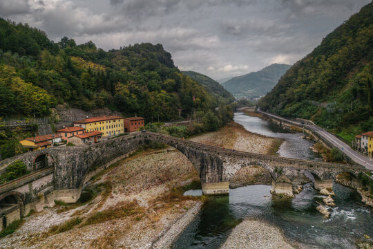 Aerial view of the historic Devil's Bridge spanning the Serchio River with surrounding lush hills and stone architecture in Borgo a Mozzano, Tuscany, Italy.