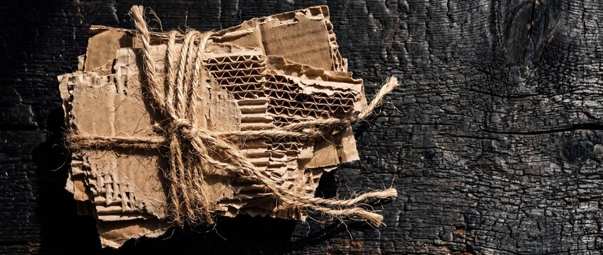 Torn Cardboard Bundle Tied with Twine on Burnt Wood