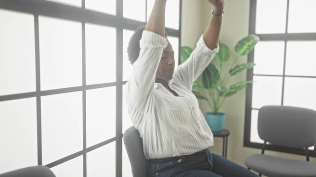 Woman sitting in chair covers face with hands and rubs eyes while waiting inside a building; fatigue relief.