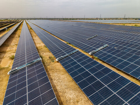Aerial view of a vast solar farm in an arid landscape featuring rows of photovoltaic panels equipped with automated cleaning robots in Rajasthan, India.