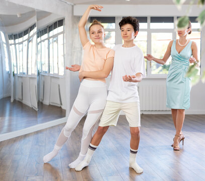 Enthusiastic teenagers, boy and girl in activewear performing elegant waltz in pair in sunny hall of dance school during lesson with female instructor..