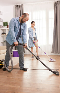 Man vacuums the floor in the foreground while a woman mops behind him, showing shared household chores and practical home cleaning teamwork, emphasizing house cleaning in everyday home life.