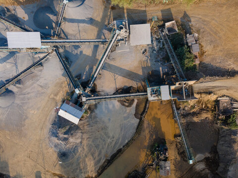 Aerial view of a sand and gravel quarry featuring conveyor belts, piles of processed material, and muddy water pools in Cilongok, Central Java, Indonesia.