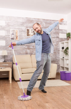 Man spreads his arms and balances beside a mop during housework, creating a playful cleaning scene about making domestic chores more enjoyable, emphasizing maintenance in everyday home life.