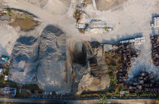 Aerial view of a sand mining quarry featuring large piles of gravel and sand, industrial machinery, and dirt tracks in Cilongok, Central Java, Indonesia.