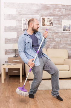 Man pretending mop is microphone while cleaning at home