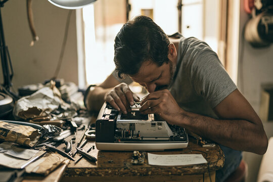 Close-up documentary shot of a skilled technician carefully soldering or repairing electronics on a cluttered workbench in a repair shop