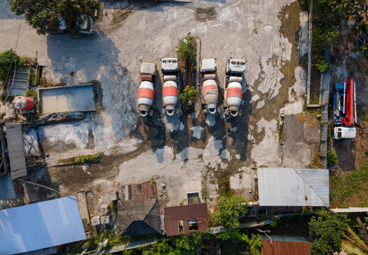 Aerial view of four concrete mixer trucks parked in an industrial yard with concrete ground and surrounding vegetation in Cilongok, Central Java, Indonesia.