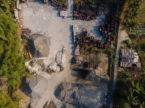 Aerial view of a sand and gravel quarry with piles of construction materials, stone blocks, and dirt paths in Cilongok, Central Java, Indonesia.