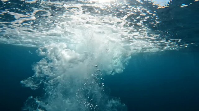 Underwater view of water splash and bubbles, deep blue ocean surface with sunlight refraction and air bubbles