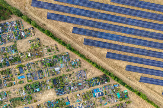Aerial view of a solar farm with rows of photovoltaic panels next to allotment gardens, showing the contrast between renewable energy and cultivated land in Hook, England, United Kingdom.