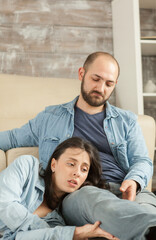 Fototapeta premium Young woman rests her head on the lap of a man as they relax together in the living room, creating a quiet scene of comfort and closeness, highlighting togetherness in a casual home setting.