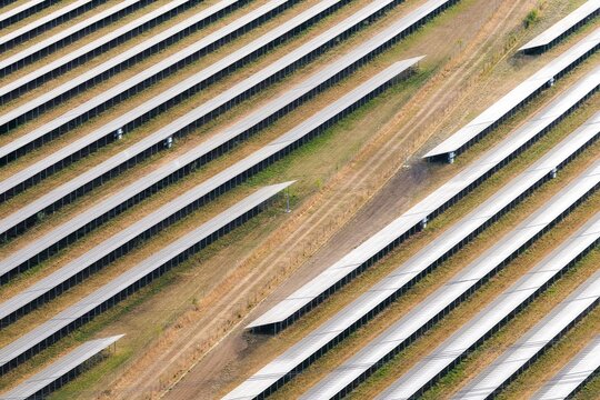 Aerial view of a solar farm with rows of photovoltaic panels arranged in parallel lines across a grassy field in Hook, England, United Kingdom.