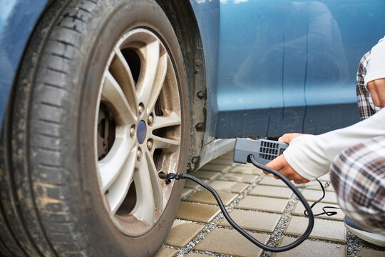 Person inflating car tire with portable air compressor beside vehicle. Concept of car maintenance