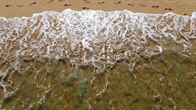 Summer text written in sand washed away by ocean waves on tropical beach