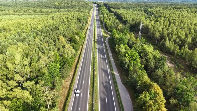 Aerial view of cars traveling along highway bordered by lush green forests. Continuous flow of vehicle traffic and natural surroundings in a serene landscape. Concept of automobile journey and trip