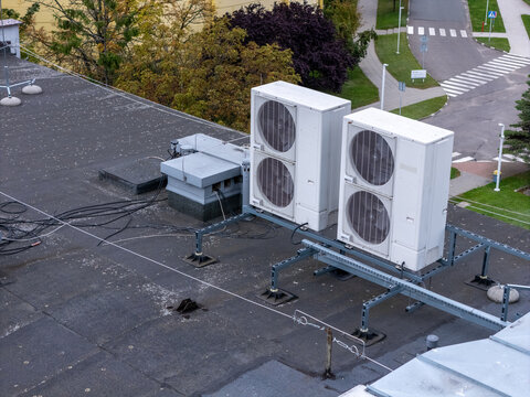 Aerial view of two large white air conditioning units installed on a flat rooftop with visible electrical cables and a road in the background in Gdansk, Poland.