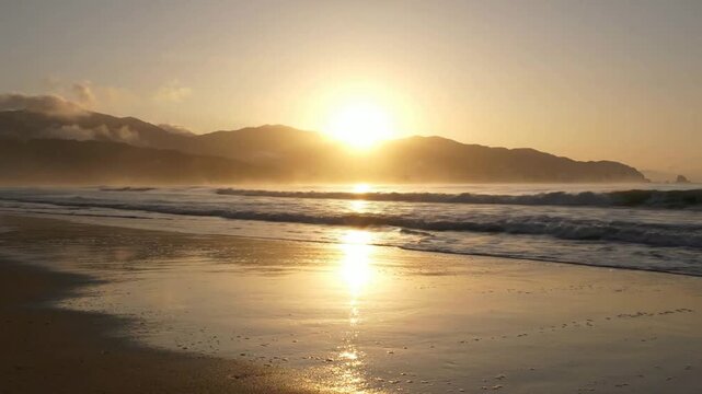 Golden sunset over tropical beach with gentle ocean waves and mountain horizon golden hour