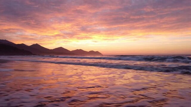 Serene ocean waves crashing on sandy beach at golden hour sunset with mountain silhouette