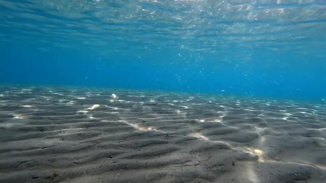 Underwater sun rays rippling on sandy ocean floor, crystal clear tropical sea background, seabed