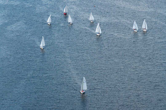 Aerial view of a sailing yacht race with multiple white sailboats gliding across the blue water, Poland.