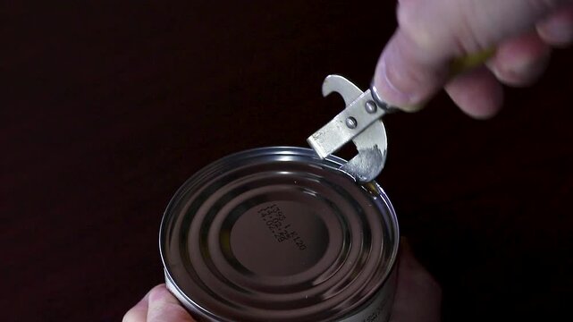 Man opening a metal tin can with a manual can opener
